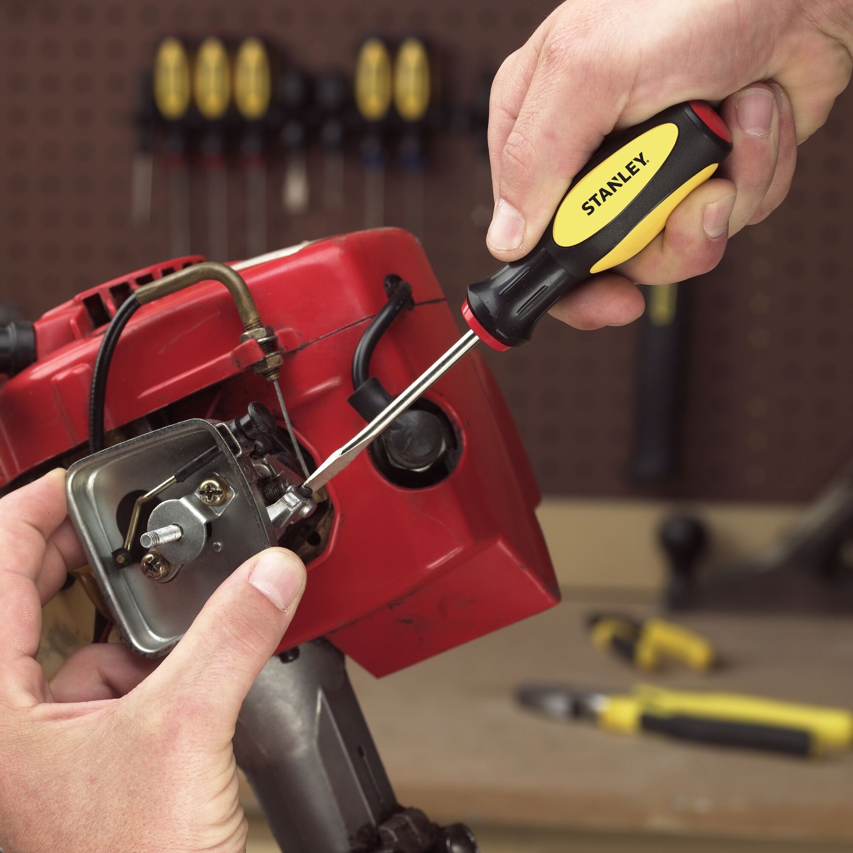 Destornillador STANLEY 60-100 usado para ajustar una pieza metálica en un motor rojo en un taller.